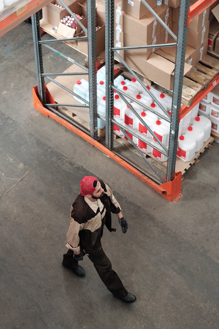 get-in-touch Warehouse worker walking among shelves stocked with packages and containers, captured from a high angle.